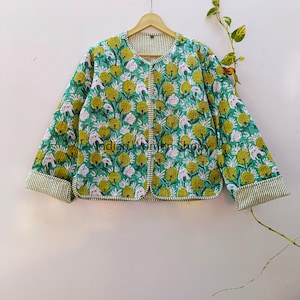 Puede incluir: Una chaqueta acolchada verde con estampado floral. La chaqueta tiene cierre de botón y un ribete a rayas.