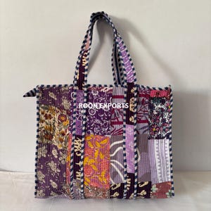 May include: A patchwork tote bag with a variety of floral and geometric patterns in shades of purple, pink, and yellow. The bag has sturdy handles and the text "ROOM EXPORTS" is visible on the front.