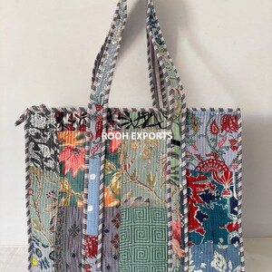 May include: A patchwork tote bag with a variety of floral and geometric patterns in shades of blue, green, red, and gray. The bag has a zipper closure and striped handles. The text "ROOH EXPORTS" is visible on the bag.