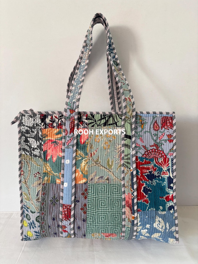 May include: A patchwork tote bag with a variety of floral and geometric patterns in shades of blue, green, red, and gray. The bag has a zipper closure and striped handles. The text "ROOH EXPORTS" is visible on the bag.