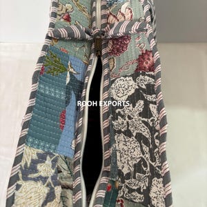 May include: Close-up of a quilted tote bag with a patchwork design. The bag features a variety of floral patterns in shades of blue, gray, and pink. A white zipper runs down the center, and the edges are trimmed with a striped fabric. The text "ROOH EXPORTS" is visible.