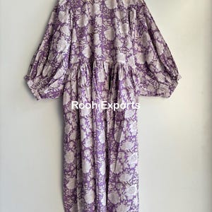 May include: A long, purple and white floral print dress with a gathered waist and puffed sleeves. The dress has a V-neckline and a relaxed fit.