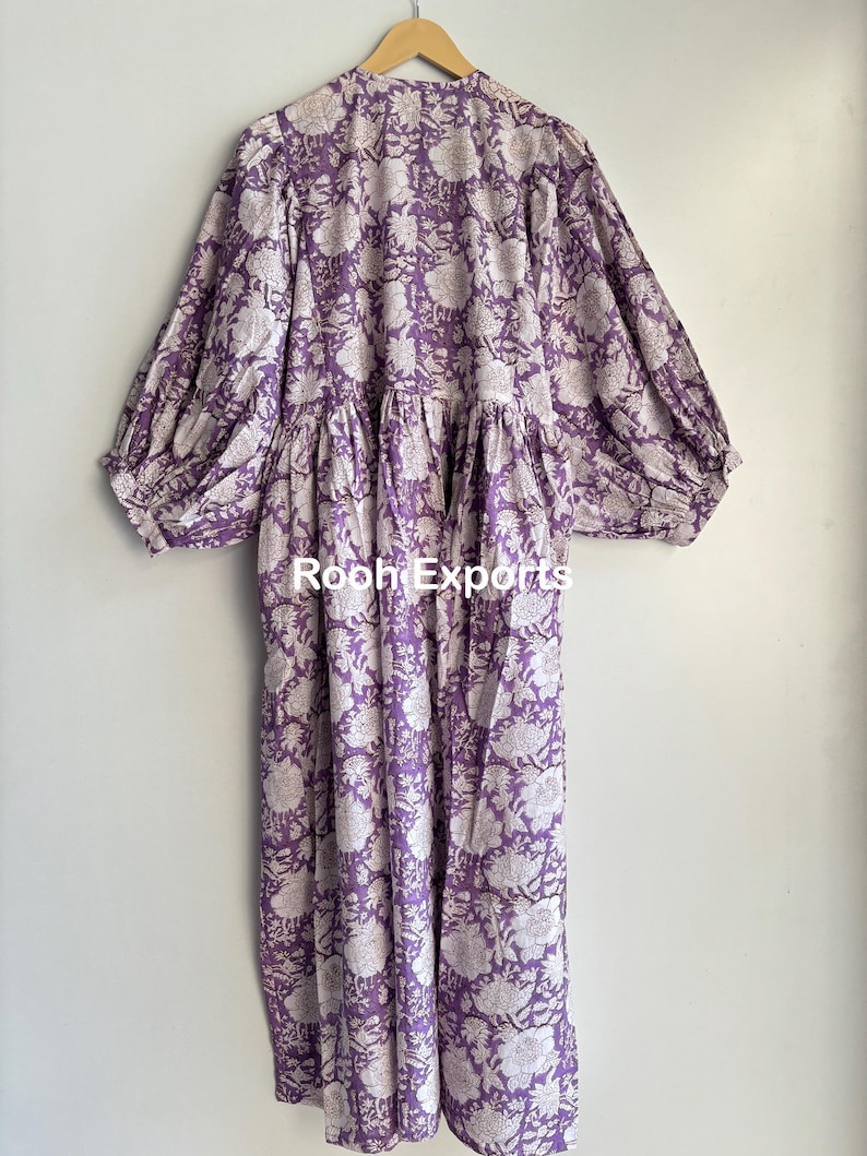 May include: A long, purple and white floral print dress with a gathered waist and puffed sleeves. The dress has a V-neckline and a relaxed fit.