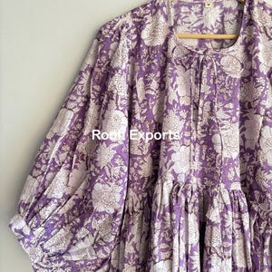 May include: A purple and white floral print cotton dress with a gathered skirt and puffed sleeves. The dress has a tie at the neckline.