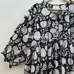 May include: A black and white cotton dress with a floral print and a tie at the neckline. The dress has a loose fit and 3/4 sleeves.
