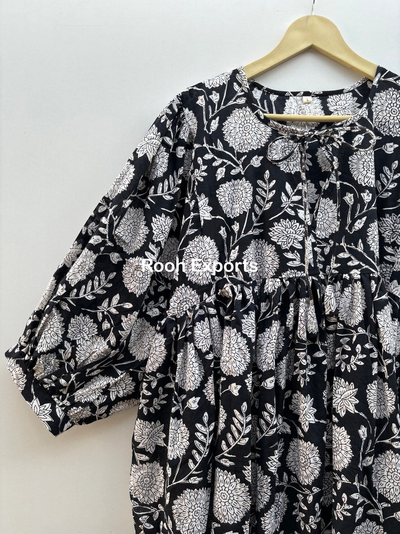 May include: A black and white cotton dress with a floral print and a tie at the neckline. The dress has a loose fit and 3/4 sleeves.