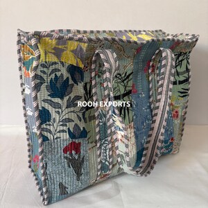 May include: A quilted tote bag with a patchwork design featuring floral patterns in shades of blue, green, yellow, and red. The bag has sturdy handles and is trimmed with a gray border. The text "ROOH EXPORTS" is visible on the bag.