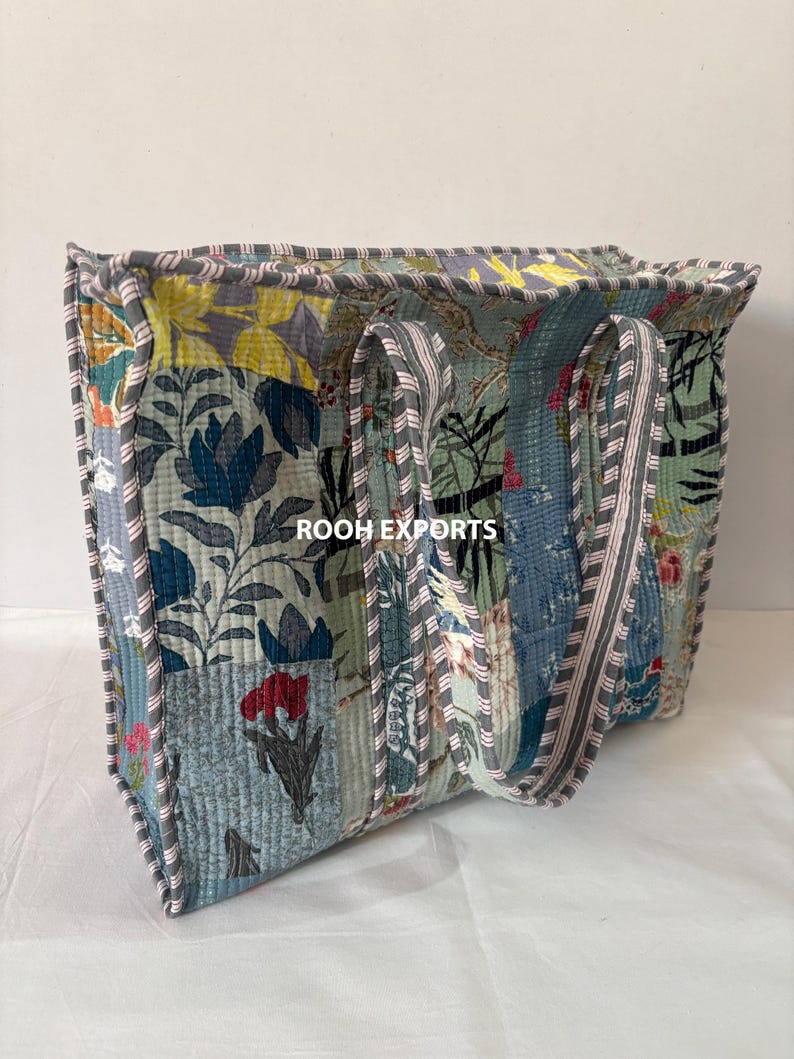 May include: A quilted tote bag with a patchwork design featuring floral patterns in shades of blue, green, yellow, and red. The bag has sturdy handles and is trimmed with a gray border. The text "ROOH EXPORTS" is visible on the bag.