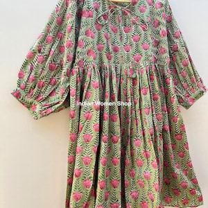 Puede incluir: Un vestido de estampado floral verde y rosa con falda fruncida y mangas 3/4. El vestido tiene un lazo en el escote y un ajuste holgado.