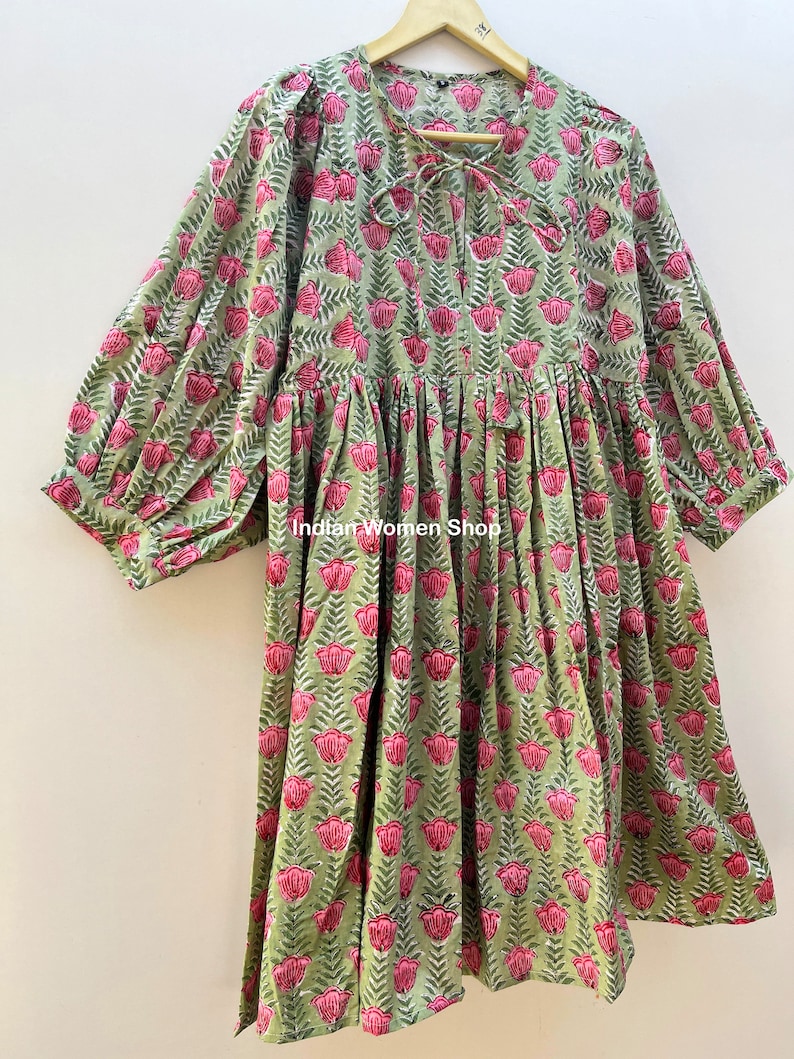 Puede incluir: Un vestido de estampado floral verde y rosa con falda fruncida y mangas 3/4. El vestido tiene un lazo en el escote y un ajuste holgado.