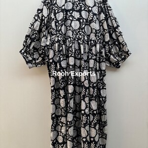 May include: A black and white floral print dress with a gathered waist and 3/4 sleeves. The dress has a round neckline and is made of cotton.