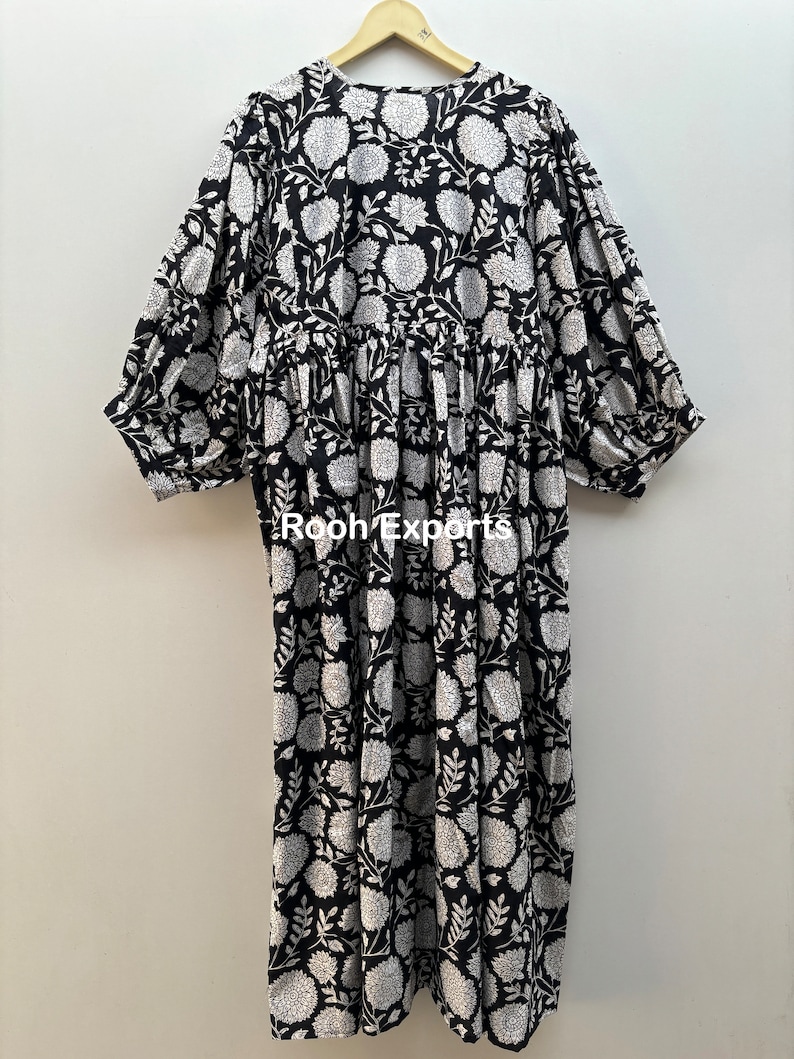 May include: A black and white floral print dress with a gathered waist and 3/4 sleeves. The dress has a round neckline and is made of cotton.