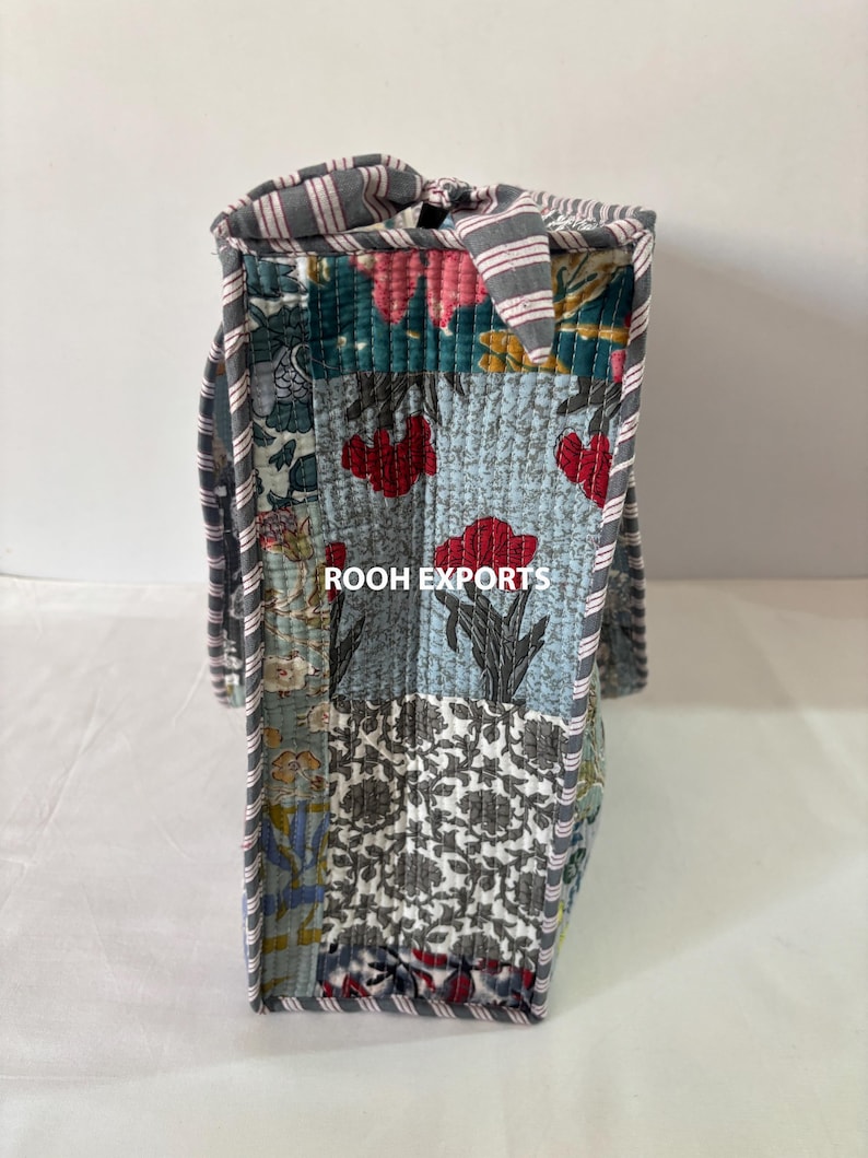 May include: A patchwork tote bag with a variety of floral and geometric patterns in shades of blue, red, and gray. The bag has a striped handle and trim, and the text "ROOH EXPORTS" is visible.