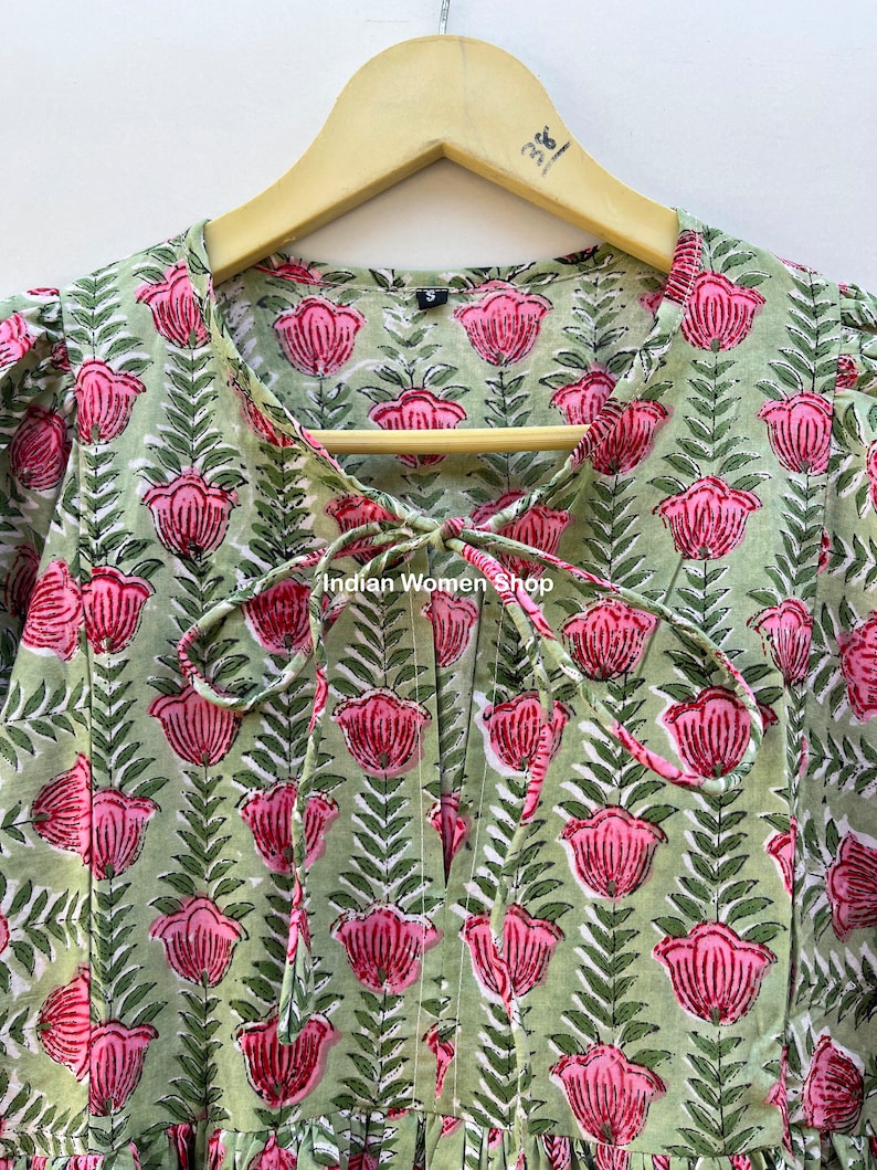 Puede incluir: Un vestido de estampado floral verde y rosa con un lazo en el escote. El vestido tiene una peque&ntilde;a etiqueta de talla en el escote. El texto "Indian Women Shop" es visible en el vestido.
