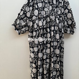 May include: A black and white floral print maxi dress with a gathered waist and 3/4 sleeves. The dress has a round neckline and a tie closure at the front.