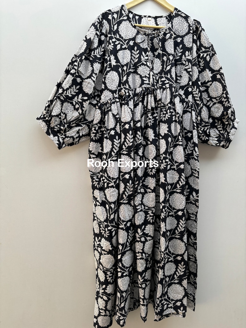 May include: A black and white floral print maxi dress with a gathered waist and 3/4 sleeves. The dress has a round neckline and a tie closure at the front.