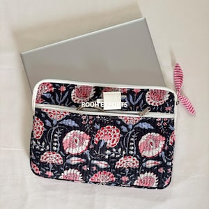 Op de afbeelding: Een zwarte laptoptas met een bloemenpatroon in roze en wit, met een witte rits en rand. De tas heeft een bijpassend roze en wit gestreept accessoire. De tekst "ROOH EXPORTS" is zichtbaar.