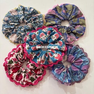 Könnte beinhalten: Sechs Stoff-Haargummis mit floralen Mustern in verschiedenen Farben. Die Haargummis zeigen rosa, rote, blaue und violette Blumenmuster mit kontrastierenden Spitzenbesätzen. Der Text "ROOH EXPORTS" ist auf einem der Haargummis zu sehen.