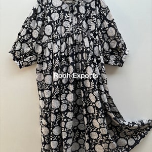 May include: A black and white floral print cotton dress with a gathered skirt and 3/4 sleeves. The dress has a round neckline and a tie at the front.