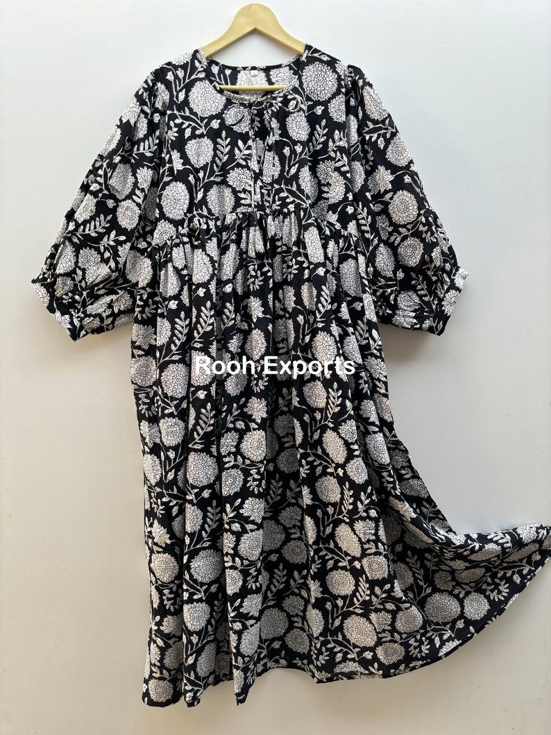 May include: A black and white floral print cotton dress with a gathered skirt and 3/4 sleeves. The dress has a round neckline and a tie at the front.