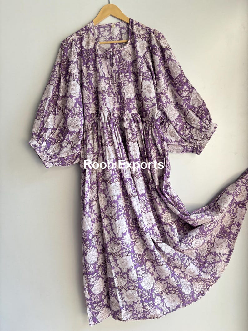 May include: A long, purple cotton dress with a white floral print. The dress has a gathered skirt and puffed sleeves.