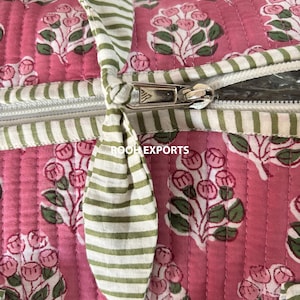 May include: Close-up of a pink quilted bag with a floral pattern in white and green. The bag features a white zipper and green and white striped handles. The text "ROOH EXPORTS" is visible.