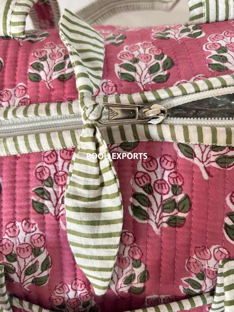 May include: Close-up of a pink quilted bag with a floral pattern in white and green. The bag features a white zipper and green and white striped handles. The text "ROOH EXPORTS" is visible.