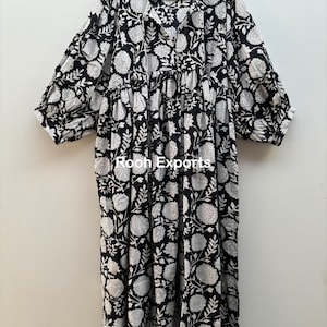 May include: A black and white floral print maxi dress with a V-neck and 3/4 sleeves. The dress has a gathered waist and a relaxed fit. The dress is made of cotton and is perfect for summer.