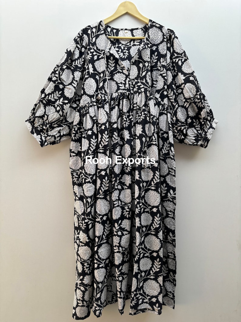 May include: A black and white floral print maxi dress with a V-neck and 3/4 sleeves. The dress has a gathered waist and a relaxed fit. The dress is made of cotton and is perfect for summer.