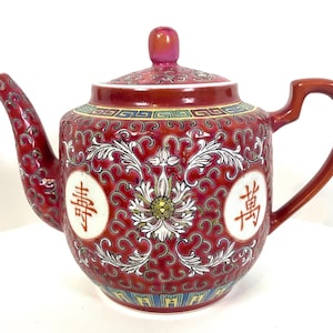 May include: Red and white porcelain teapot with intricate floral designs and Chinese characters. The teapot has a lid and a spout.