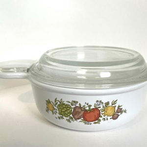 May include: White ceramic casserole dish with a glass lid. The dish has a floral design with a variety of vegetables and herbs.