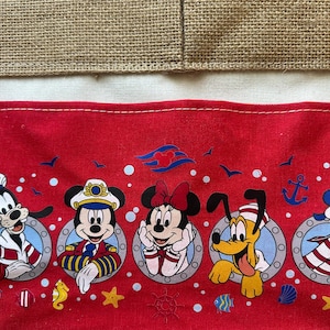 May include: Red fabric featuring Disney characters Goofy, Mickey Mouse, Minnie Mouse, Pluto, and Donald Duck in sailor outfits. The design includes anchors, stars, and other nautical elements, with a burlap and white fabric background.