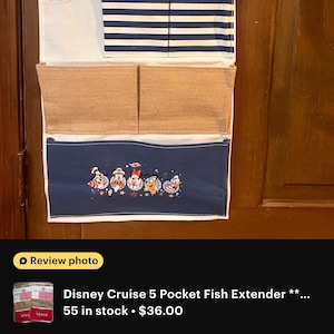 May include: A multi-pocket organizer with a Disney Cruise Line theme. The top section is off-white with two small hooks. Below is a section with navy blue and white stripes. The bottom section is navy blue with embroidered Disney characters.