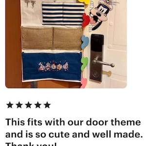 May include: A hanging organizer with multiple pockets. The top section has a Disney Cruise Line logo and two small hooks. Below are sections with blue and white stripes, two tan pockets, and a blue embroidered section with Disney characters. The door has Disney character stickers.