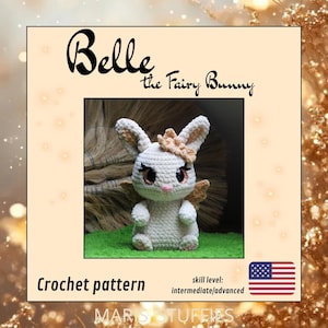 Op de afbeelding: Een gehaakt feeënkonijn genaamd Belle met grote oren, vleugels en een bloemenkroon. Het konijn is wit met bruine accenten en bruine ogen. De afbeelding bevat de tekst "Belle the Fairy Bunny" en "Crochet pattern". Vaardigheidsniveau: gemiddeld/gevorderd.