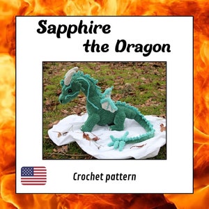Puede incluir: Patrón de crochet para un dragón verde y azul llamado Sapphire. El dragón está sentado en un paño blanco con hojas a su alrededor. El patrón está disponible para su compra.