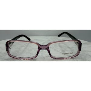 May include: Rectangular Tom Ford eyeglasses with a translucent purple frame and black temples. The lenses are clear, and the Tom Ford logo is visible on the right lens.