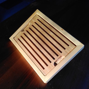 Puede incluir: Una tabla de cortar de madera con un marco y ranuras para sujetar el pan. La tabla es de color marrón claro y tiene un acabado de madera natural.