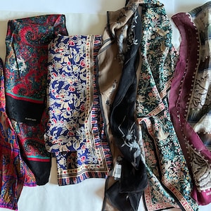 May include: A collection of six rectangular scarves featuring diverse patterns including red and blue paisley, floral motifs on navy, black and beige botanical prints, and a burgundy-bordered scarf with a blue and white abstract geometric design.