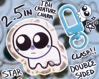 May include: A 2.5 inch double-sided charm featuring a white cartoon creature with large eyes. The front side has a holographic finish and the back side is plain. The charm comes with a blue metal clasp.