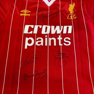 May include: Red and white striped soccer jersey with the logo "L.F.C." and the sponsor "Crown paints". The jersey has several signatures in black ink.