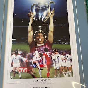 Puede incluir: Una foto enmarcada de Tony Morley, un ex jugador del Aston Villa, sosteniendo el trofeo de la Copa de Europa. La foto está firmada por Tony Morley e incluye el texto "Tony Morley Aston Villa 1979-1983 League Apps 137 Goals 25".