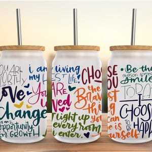 Puede incluir: Tres vasos de vidrio con tapas de bambú y pajitas de acero inoxidable. Cada vaso tiene una cita inspiradora diferente en varios colores. Las citas incluyen frases como "Eres digno de amor" y "Elige ser feliz."