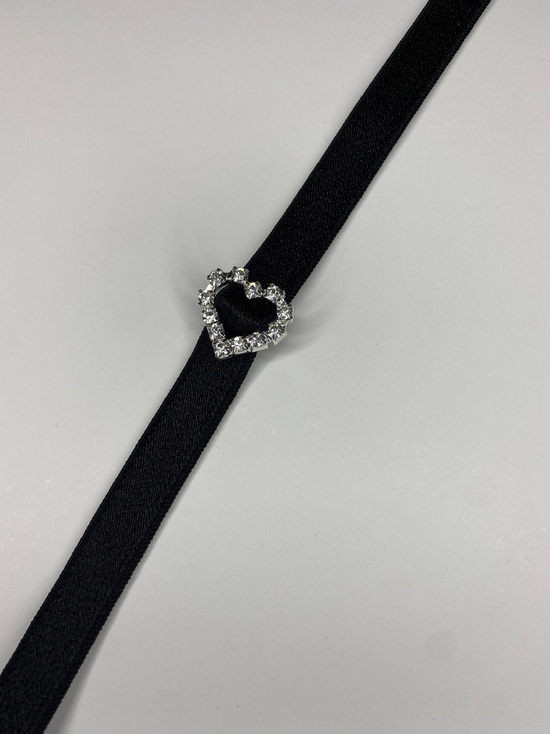 May include: A black ribbon with a silver heart-shaped buckle adorned with clear rhinestones.