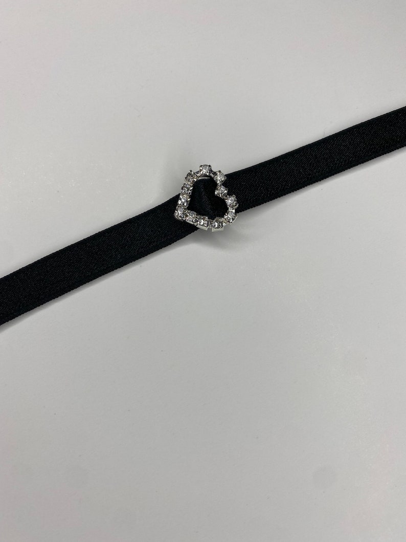 May include: A black choker necklace with a silver heart-shaped charm encrusted with clear rhinestones.