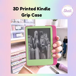 Op de afbeelding: Een 3D-geprinte Kindle-gripcase met een groen frame en roze zijkant. Het Kindle-scherm toont een zwart-wit afbeelding. De tekst op de afbeelding luidt "3D Printed Kindle Grip Case".