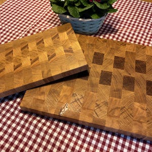 May include: Three wooden butcher block cutting boards with a checkerboard pattern. The boards are made of light brown wood and are rectangular. The boards are on a red and white checkered tablecloth.