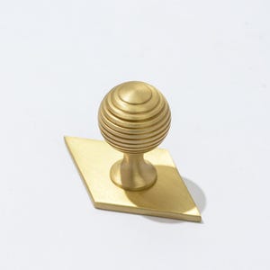 May include: A gold-toned cabinet knob with a round, ribbed top and a diamond-shaped base.