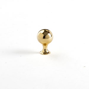 May include: A shiny, gold-colored cabinet knob with a spherical top and a pedestal base. The knob is designed for furniture and has a polished finish, reflecting light. It is a decorative hardware element.