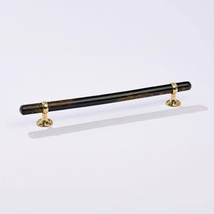 May include: A black and gold door handle with a long, cylindrical shape. The handle is made of wood and has a brass finish.